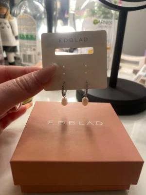 Edblad örhängen  - Bilderna visar ett par örhängen från Edblad med vita pärlor och silverfärgade örhängen med glittriga stenar. Fick i Julkapp men blev fel färg! Så oanvända. Lägger ut dom här i hopp om att nån köper så jag kan köpa dem i rätt färg! Original priset är 400 kr men kan tänka mig att gå ner något. 