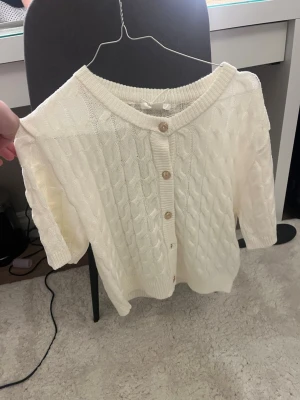 Vit kabelstickad kofta Gina Tricot - Säljer en vit kabelstickad kofta från Gina Tricot i storlek 170. Koftan har korta ärmar, rund halsringning och snygga knappar framtill. Perfekt till lager på lager och enkel att matcha med olika outfits.