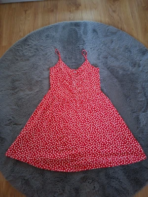 Röd blommig sommarklänning INSIDE - Säljer en röd kortklänning från INSIDE i storlek M med vita blommor över hela tyget. Klänningen har smala axelband och en lätt utställd form som ger en skön och avslappnad vibe. Perfekt för varma dagar och har en riktigt söt look.