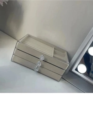 Beige smyckesförvaring med glas och kristallknoppar - Snygg och stilren smyckesförvaring i beige med tre lådor, glaslock och glittriga kristallknoppar. Insidan har fack för ringar, örhängen och andra accessoarer. Perfekt för att hålla ordning på dina smycken och ge en lyxig känsla till rummet.