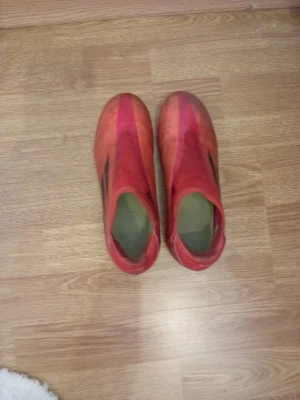 Röda adidas fotbollsskor X - Säljer ett par röda adidas X fotbollsskor med svarta detaljer och vit sula med röda dobbar. Skorna har en strumpliknande passform utan snörning och är tillverkade i syntetmaterial med meshpartier för extra ventilation. Perfekta för dig som vill sticka ut på planen.