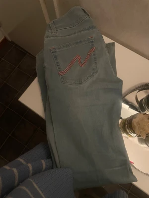 Ljusblå jeans från Nelly med broderi - Säljer ett par ljusblå jeans från Nelly med snyggt rött broderi på bakfickan. Jeansen har klassisk femficksdesign, raka ben och detaljer i röd tråd vid knapphål och sömmar. Perfekta för dig som vill ha en unik touch på din denimstil. PRIS KAN DISKUTERAS 