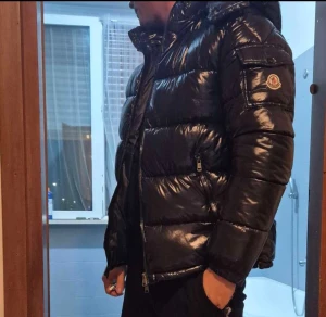 Svart Moncler pufferjacka med huva - Säljer en svart, glansig pufferjacka från Moncler med huva och dragkedja framtill. Jackan har Moncler-logga på ärmen, praktiska fickor med dragkedja och en schysst oversized look. Perfekt för kalla dagar och riktigt snygg till streetwear-stilen.