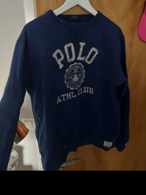 Marinblå sweatshirt Polo Ralph Lauren - Säljer en marinblå sweatshirt från Polo Ralph Lauren i storlek L. Tröjan har tryckt logga och text på bröstet, rund halsringning och långa ärmar. Klassisk college-look och mjukt bomullsmaterial som är skönt att bära.