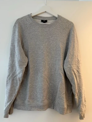 Grå sweatshirt från H&M, storlek M - En basic grå sweatshirt från H&M i storlek M. Tröjan har rund halsringning, ribbade muddar vid ärmslut och nederkant samt en avslappnad passform. Perfekt till chill dagar och enkel att matcha med allt.