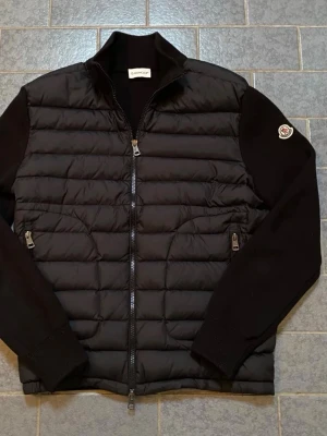 Svart Moncler pufferjacka med stickade ärmar - Säljer en svart pufferjacka från Moncler med quiltad front och stickade ärmar. Jackan har dragkedja framtill, två sidofickor med dragkedja och Moncler-logga på ena ärmen. Perfekt för dig som vill ha en stilren och exklusiv look. Pris kan ej diskuteras, skriv gärna för frågor&bilder äkta kvitto finns. Skick 9,5/10