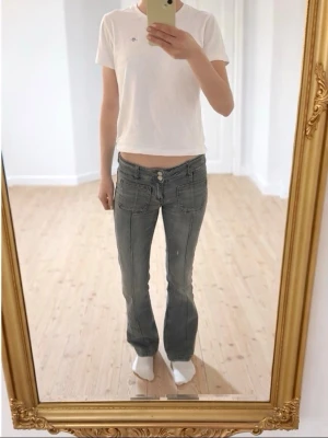 Grå lågmidjade jeans från Gina Tricot - Säljer ett par grå jeans från Gina Tricot i storlek 158. De har låg midja, bootcut och dubbla knappar framtill. Jeansen har klassiska fickor både fram och bak och är tillverkade i ett mjukt jeansmaterial.