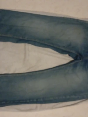 Blå jeans med broderade bakfickor - Säljer ett par ljusblå jeans med snygga broderade detaljer på bakfickorna. Jeansen har klassisk femficksdesign och raka ben. Materialet är slitstarkt jeans och färgen har en tvättad look med ljusare partier. Perfekta för en avslappnad stil.