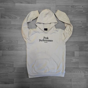 Peak Performance White Hoodie – Size 170 (Bra skick) 🔥 - Klassisk Peak Performance hoodie i ren vit med fet svart broderad "Peak Performance Est. 1986" print på ryggen – tidlös outdoor/premium streetwear-känsla. Mjuk, mysig bomullsblandning fleece-tyg, dragsko-huva, kangaroo-ficka, ribbade muddar och fåll. Ren, mångsidig och perfekt för layering eller vardagsbruk – ikonisk skandinavisk kvalitetsmärke!. Size 170. Sitter som en S