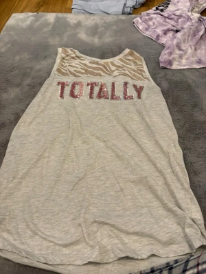 Beige zebramönstrad linnetopp H&M - Säljer en beige ärmlös linnetopp från H&M med zebramönstrad mesh upptill och paljetter i rosa och silver som stavar 'TOTALLY' på bröstet. Toppen har en avslappnad passform och är perfekt för dig som gillar statementplagg.