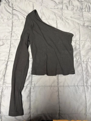 Svart oneshoulder topp från NA-KD - Säljer en svart ribbad oneshoulder topp från NA-KD i storlek S. Toppen har lång ärm på ena sidan och är croppad i modellen. 