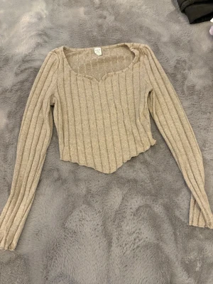 Beige ribbad topp från SHEIN Teen - Säljer en beige ribbad topp från SHEIN Teen i storlek 10-11 år. Toppen har lång ärm, v-ringad hals och croppad asymmetrisk nederkant. Materialet är mjukt och stretchigt, perfekt för en chill och trendig look. 