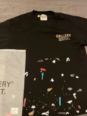 Svart Gallery Dept t-shirt Tokyo - Svart t-shirt från Gallery Dept. med trycket 'TOKYO, JAPAN' på bröstet och färgstänk i vitt, blått, rött, guld och lila över framsidan. Klassisk passform och rund hals. Perfekt för dig som gillar streetwear och unika prints. Jag e 180 och väger 65kg.