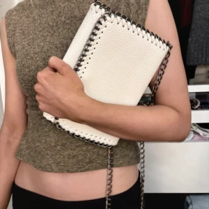 Vit axelväska med kedjedetaljer - Säljer en snygg vit axelväska i skinnimitation med grov silverfärgad kedja och dekorativa sömmar längs kanterna. Väskan har en stilren, rektangulär form och känns både trendig och edgy. Perfekt för dig som vill ha en statementväska till din outfit.