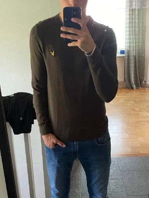 Brun stickad tröja från Lyle & Scott - Säljer en brun stickad tröja från Lyle & Scott med den klassiska gula loggan på bröstet. Tröjan har rund halsringning och långa ärmar, perfekt för lager på lager under kyligare dagar. Enkel och stilren design som funkar till det mesta.