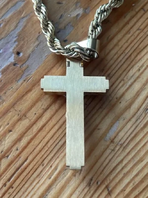 Guldig korshalsband med 18karat guldplaterat - Säljer ett chunky halsband i guldton med tvinnad kedja och stort korshänge. Hänget har en 3D-detaljerad Jesusfigur och texten INRI upptill. Korset har en borstad finish och svarta detaljer som ger en cool kontrast. Perfekt accessoar för dig som vill sticka ut.