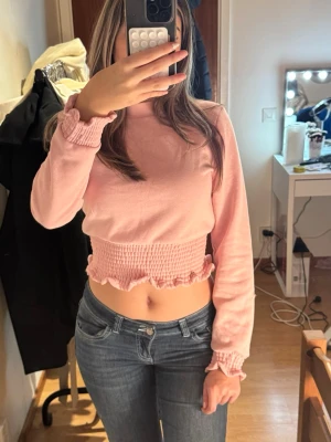 Rosa croppad långärmad topp - Supersöt ljusrosa croppad topp med lång ärm. Toppen har smockad midja och ärmslut med volangdetaljer. Helt ny!