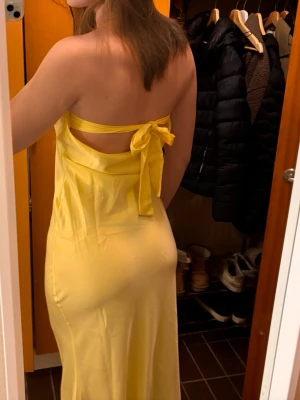 Gul axelbandslös långklänning - Säljer en superfin gul långklänning perfekt för balen! Oandvänd med prislapp kvar. Bara dubbelfodrad över bysten. Nypris 709kr