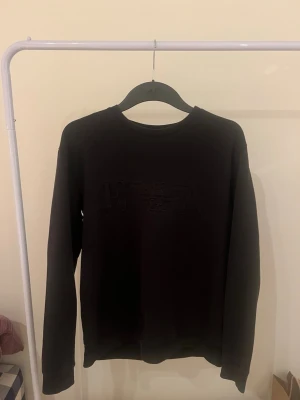 Svart tröja från Emporio Armani - Säljer en svart sweatshirt från Emporio Armani med diskret broderad logga på bröstet. Tröjan har rund halsringning och långa ärmar. Perfekt för dig som gillar stilrena och exklusiva plagg.