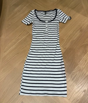 Randig kortklänning från H&M Divided - Superfin kortklänning från H&M Divided i vitt och marinblått med klassiskt randigt mönster. Klänningen har rund halsringning, korta ärmar och knappar framtill. Materialet är ribbat och stretchigt, vilket gör den både bekväm och snygg.OANVÄND 