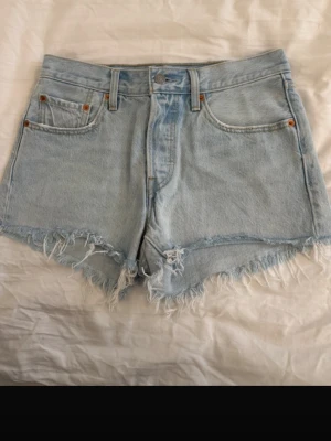 Levi's 501 ljusblå jeansshorts - Ljusblå Levi's 501 jeansshorts med hög midja. Klassisk femficksmodell med Levi's patch bak och röd etikett på ena bakfickan. Perfekta för sommaren☺️
