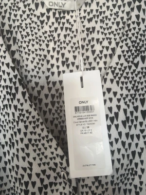 Vit kortklänning med hjärtmönster från ONLY - Supersöt vit kortklänning från ONLY med svart hjärtmönster. Klänningen har v-ringning, korta ärmar och ett lätt, luftigt tyg som känns perfekt för varma dagar. Resår i midjan ger en snygg siluett och den är riktigt bekväm att bära.