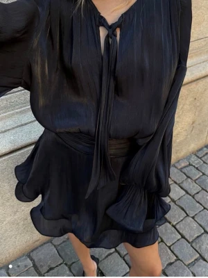 Svart kort klänning med volangärm - Supersnygg svart kort klänning i glansigt material med volangärmar! Endast använd en gång