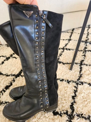 Svarta stövlar Laura Biagiotti, strl 41 - Snygga svarta stövlar från Laura Biagiotti i storlek 41. Skorna har en mix av skinn och mocka, dekorerade med nitar längs dragkedjan och en liten klack. Perfekta till höst och vinter för en edgy look.