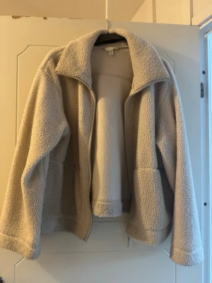 Beige teddyjacka från H&M  - Mysig beige teddyjacka från H&M i storlek XL. Jackan har dragkedja framtill, stora fickor och en hög krage. Perfekt för kyliga dagar och ger en chill oversized look. Materialet är fluffigt och mjukt, vilket gör den superbekväm att bära.