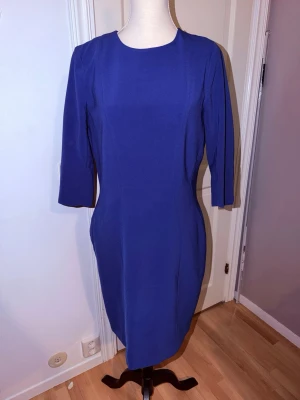 Blå figurnära klänning från H&M - Snygg blå klänning från H&M med figurnära passform och trekvartsärm. Klänningen har rund halsringning och dragkedja bak för enkel påklädning. Perfekt för dig som gillar stilrena och klassiska plagg.