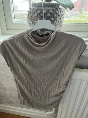 Beige topp med rynkad sida 157 - Säljer en beige topp från 157 i storlek S. Toppen är rundhalsad och är ärmlös med snygga rynkade detaljer längs ena sidan. Tillverkad i mjukt och stretchigt material som sitter skönt på kroppen. Perfekt att styla med jeans eller kjol.