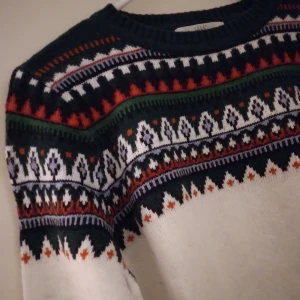 Mönstrad stickad tröja / jultröja från H&M L.O.G.G, Medium, NYSKICK - Stickad tröja / jultröja från H&M L.O.G.G. i storlek M. Tröjan är vit med flerfärgat mönster över bröst, axlar och nederkant. Rund hals och långa ärmar. Perfekt för dig som gillar klassiska vintervibbar och snygga detaljer. Nyskick, endast använd 1 gång. Felfri.