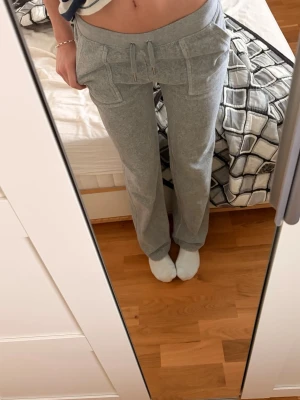 Grå Juicy Couture - Grå mjukisbyxor från Juicy Couture i storlek XS. Byxorna har snörning i midjan, stora fickor fram och bak med lock och knappar💞väldigt snygga y2K stil❤️innerbenslängd:81cm     Waist:67,5