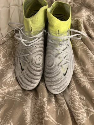 Nike Phantom Luna fotbollsskor gul/vit - Säljer ett par Nike Phantom Luna Elite fotbollsskor i vitt och neongult med stickad ovandel och snörning. Skorna har rund tå, platt sula med dobbar och coola cirkulära mönster på ovandelen. Perfekta för dig som vill sticka ut på planen. Pris kan diskuteras 