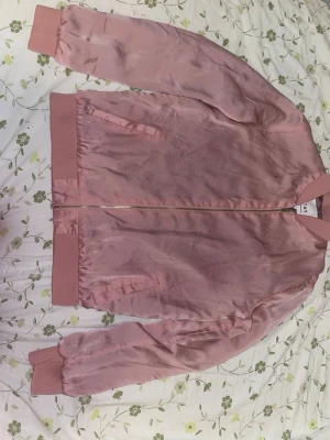 Rosa satin bomberjacka från STAY - Säljer en snygg rosa bomberjacka från STAY i satinliknande polyester. Jackan har ribbade muddar, dragkedja framtill och två fickor. Perfekt för dig som vill ha en stilren och trendig jacka med lite glansig finish.
