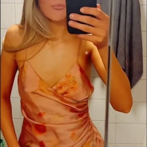 Blommig omlott linnetopp i satin - Säljer en superfin ljusrosa omlott linnetopp med tunna axelband och blommigt mönster i orange, grönt och gult. Toppen har draperad effekt på sidan och är gjord i glansigt satinliknande material som ger en lyxig känsla. Perfekt för sommarens alla tillfällen!