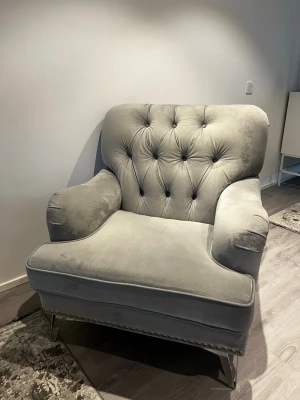 Soffa - Säljer en stilren och bekväm fåtölj i mjuk grå sammet. Fåtöljen har ett klassiskt, tidlöst utseende med dekorativa knappar i ryggstödet och nitar framtill som ger en exklusiv känsla. Stadiga ben i krom/metall ger både stabilitet och modern design.  Fåtöljen är bekväm att sitta i och passar perfekt i vardagsrum, sovrum eller som accentfåtölj. Använd men i mycket fint skick, inga skador – endast normala märken i sammeten som uppstår vid användning. Vid snabb afär kan vi diskutera om priset