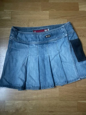 Lågmidjad jeanskjol från Guess - Säljer en snygg blå jeanskjol från Guess med plisserad design och rå kant nertill. Kjolen har en cool kontrastficka i mörkare denim på sidan och detaljerade sömmar. Storlek M, men skulle säga att den sitter som S! Kontakta vid frågor🤗