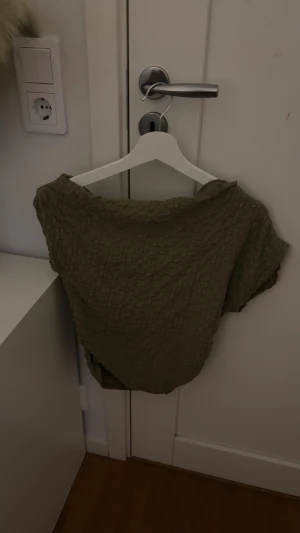 Olivgrön kortärmad linnetopp - Säljer en olivgrön linnetopp med korta ärmar och en bred halsringning. Toppen har en snygg, strukturerad yta med rutigt mönster och är tillverkad i ett lätt och luftigt material som passar perfekt till varma dagar.