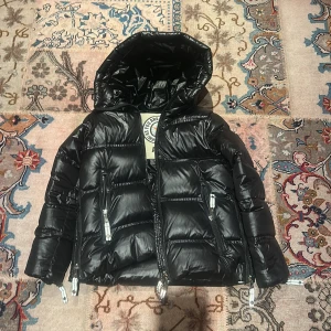 Svart pufferjacka från Caya, modell Erikas Lux - Säljer en svart pufferjacka med glansig finish från C.A.Y.A Jackan har huva, flera dragkedjor och fick den för ett år sen, knappt använd. Perfekt för alla dagar under kalla vinter halvåret. 