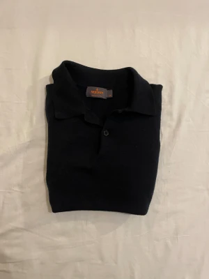 Svart merinoull pikétröja Morris XS - Svart långärmad pikétröja från Morris i 100% merinoull. Klassisk krage och knapp framtill, perfekt för dig som gillar stilrena och tidlösa plagg. Mjuk och tunn stickning som känns skön mot huden. Passar dig som vill ha en clean look. Obs jag har lagat ett hål på bröstet.