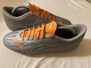 Puma Ultra grå/orange fotbollsskor - Säljer ett par Puma Ultra fotbollsskor i storlek 44. Skorna är grå med orange detaljer, snörning och Puma-logga på sidan och tungan. Ovandelen har ett mönstrat syntetmaterial och sulan har fasta dobbar för bra grepp på planen. Riktigt snygg design för dig som vill sticka ut. Använda max 3 gånger köpta för 950kr. Pris kan diskuteras. Tveka inte på att skriva.