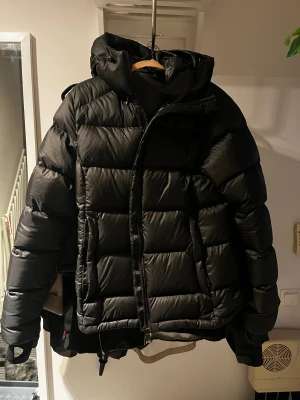 Svart pufferjacka från Everest - Svart vinterjacka från Everest med huva och dragkedja framtill. Jackan har en quiltad design med breda kanaler och två sidofickor. Materialet är syntet och varm, perfekt för kalla dagar❄️🥰. Snygg och enkel stil som funkar till det mesta.💕💕Säljer pga att den inte passar längre. Har bara använts en vinter🤍🤍 Ordinarie pris: 2499kr