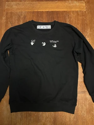 Off-White svart sweatshirt med silvertryck - Svart sweatshirt från Off-White med vit logga och handgrafik på bröstet. Baksidan har ett stort, unikt silvermönster i Off-Whites klassiska korsdesign. Tröjan har rund hals, långa ärmar och är gjord i mjuk bomull. Perfekt för dig som gillar streetwear med edge.