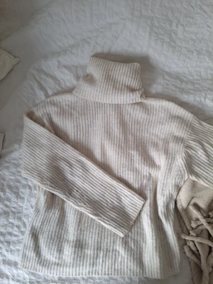 Ribbad polotröja i ljus beige - Säljer en mysig ribbad polotröja i ljus beige med lång ärm och hög krage. Tröjan är stickad och har en skön, loose passform som är perfekt för kyliga dagar. Enkel att matcha med jeans eller kjol för en chill look.