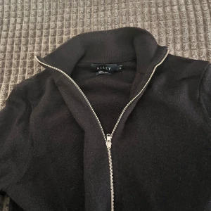 Svart hel-zip tröja i merinoull från Riley - Svart hel-zip från Riley i mjuk merinoull med hel dragkedja framtill och hög krage. Stilren och enkel design, perfekt att slänga på sig när det är lite kyligt. Långärmad och med en otroligt skön passform som sitter snyggt på kroppen. Passar mig perfekt som är runt 179-181!! Tröjan är använd endast en gång tidigare.