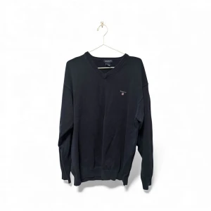 Svart v-ringad tröja från GANT - Svart v-ringad tröja från GANT i storlek L. Klassisk design med diskret logga broderad på bröstet. Tröjan har långa ärmar och ribbade muddar vid hals, ärmslut och nederkant. Perfekt för dig som gillar stilrena och tidlösa plagg.