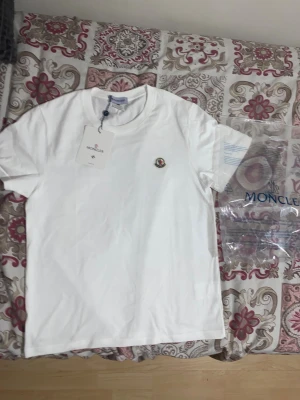 Vit Moncler t-shirt i bomull - Vit t-shirt från Moncler i mjuk bomull med klassisk rund hals och korta ärmar. Diskret Moncler-logga broderad på bröstet. Enkel och clean design som passar perfekt till jeans eller shorts.