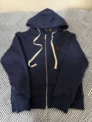 Mörkblå hoodie från Polo Ralph Lauren - Snygg mörkblå hoodie från Polo Ralph Lauren med klassisk röd broderad logga på bröstet. Helt ny och oanvänd. Storleken är S men passar xs.