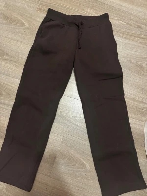 Bruna mjukisbyxor  - Mörkbruna mjukisbyxor med ribbad midja och snörning. Byxorna har raka ben och sidofickor, perfekta för chill dagar. Tillverkade i mjukt bomullsmaterial för extra komfort. 